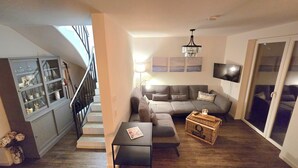 A living room with a grey sofa, a coffee table, a TV, and a staircase leading to another level. - Cozy half of the house near the lake with barbecue, within walking distance of the bathing area & Satama (Wendisch Rietz)