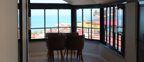 Un comedor con vistas al mar, un balcón con barandilla y una puerta que da a otra habitación.