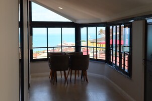 Un comedor con vistas al mar, un balcón con barandilla y una puerta que da a otra habitación.
