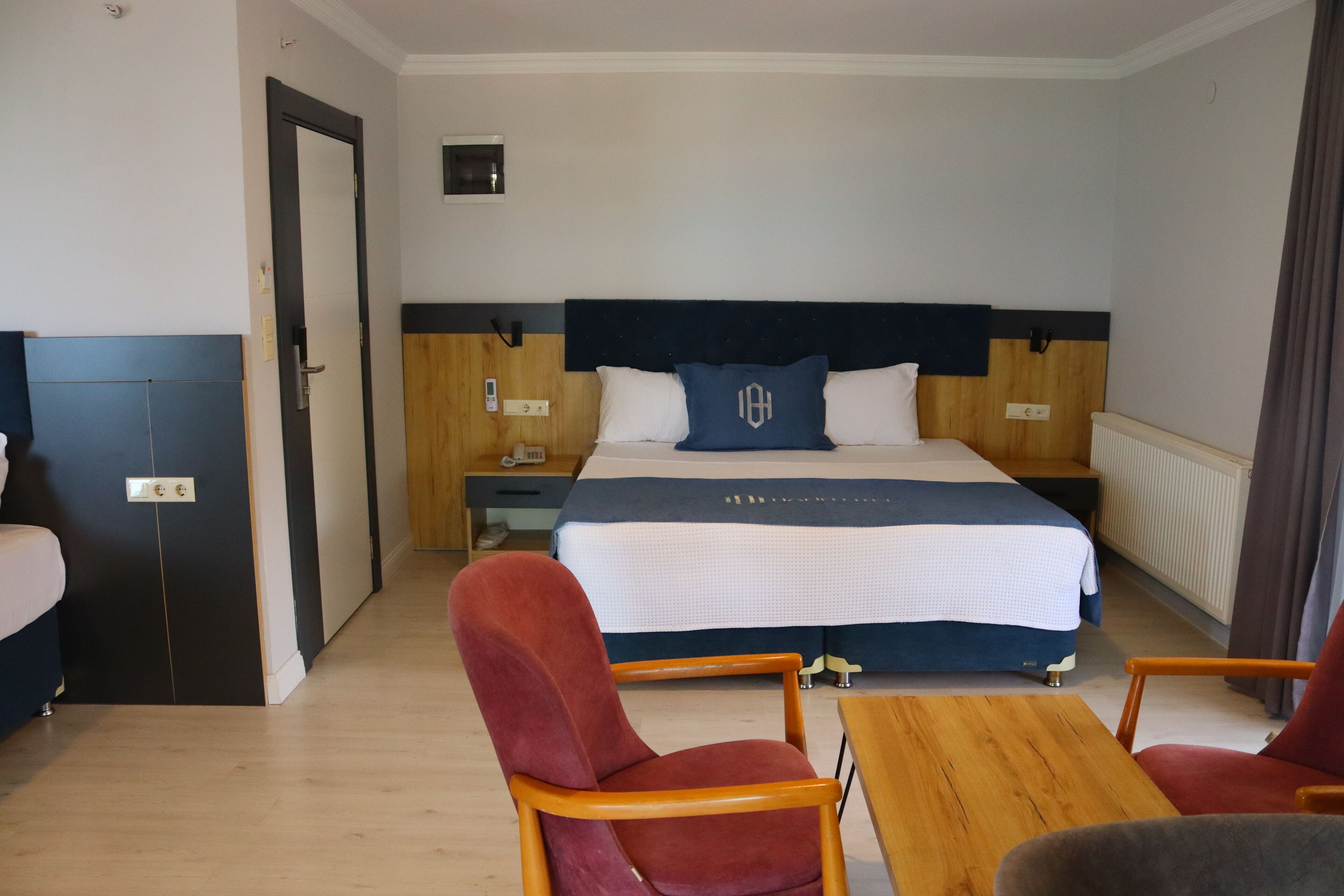 A hotel room with a large bed, wooden headboard, two bedside tables, a nightstand, a red chair, and a wooden table.