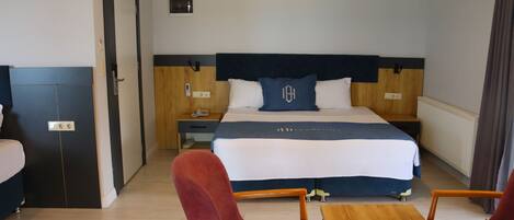 Una habitación de hotel con una cama grande, cabecero de madera, dos mesitas de noche y una silla roja, además de una mesa de madera.