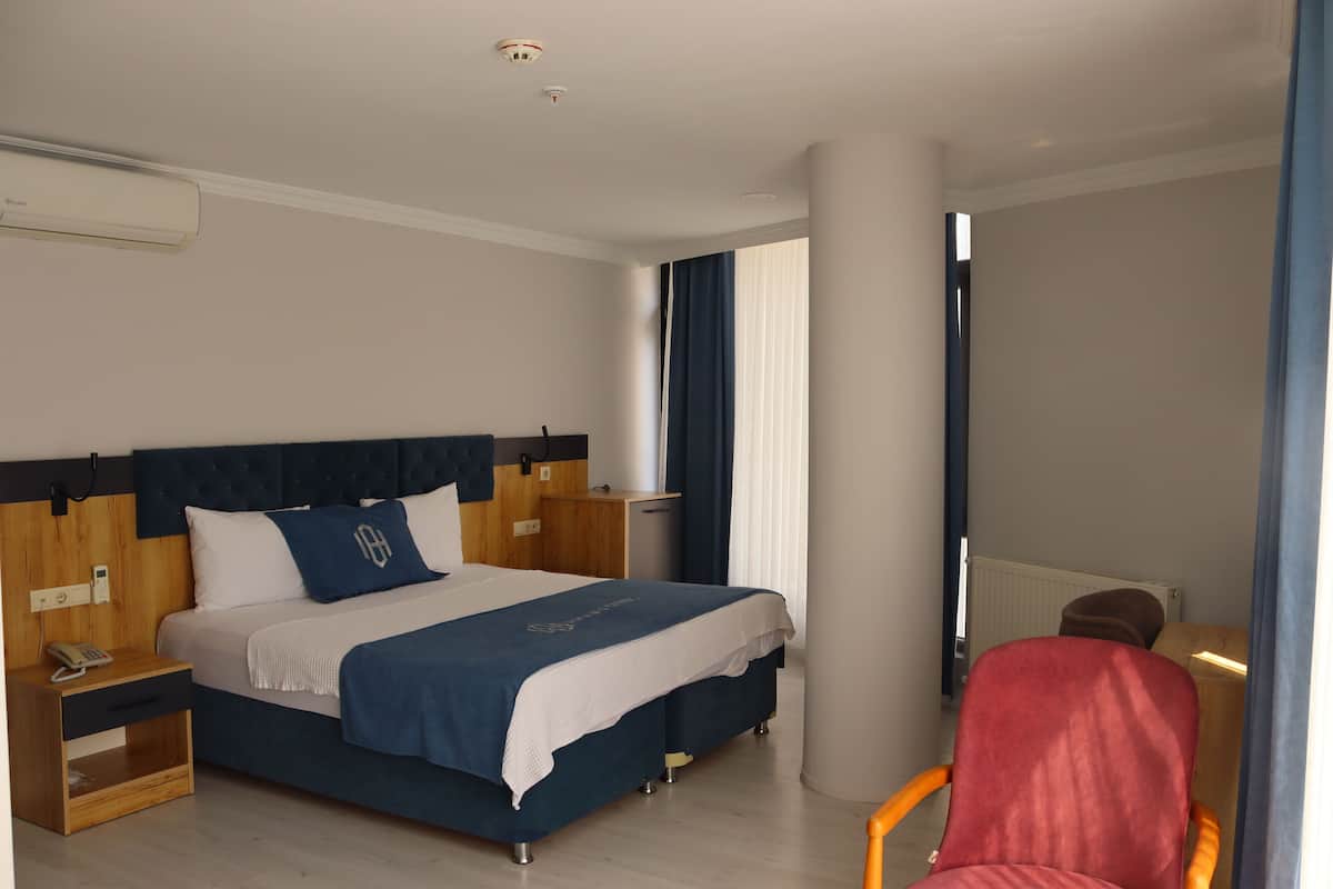 A modern hotel room with a large bed, a nightstand with a phone, a red chair, and a window with curtains.