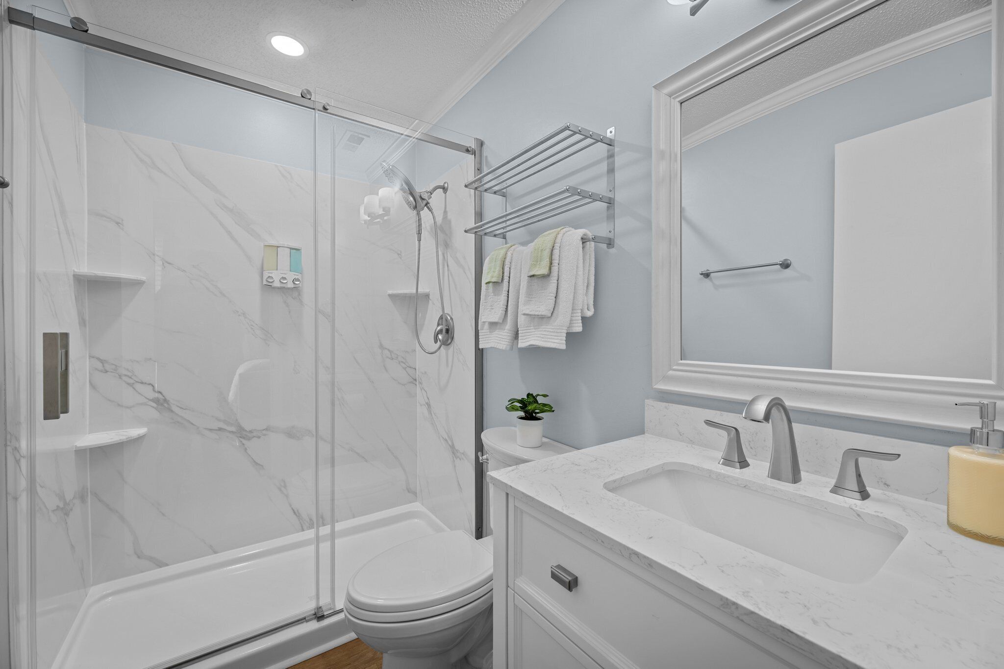Un baño moderno con ducha envuelta en vidrio, inodoro blanco, lavamanos con encimera de mármol y un espejo grande.
