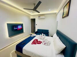 A hotel room with a bed, a ceiling fan, an air conditioning unit, a mounted TV, and a framed picture on the wall.
