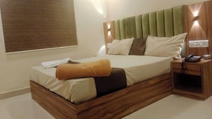 A modern hotel room with a wooden bed frame, a green upholstered headboard, and a bedside table with a phone and a lamp. - Hotel Stay Inn (Mumbai)
