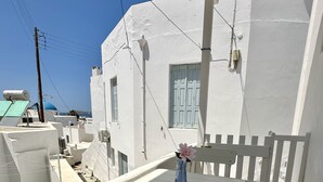Ein weißer Balkon mit Tisch und Stuhl, einer kleinen Vase mit einer Blume und Blick auf ein blaues Kuppelgebäude im Hintergrund.