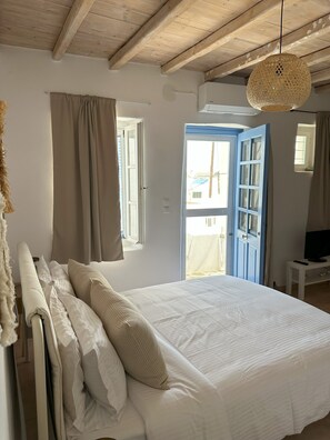 A bedroom with a large bed, a wooden ceiling, a window with curtains, and a television on a small table. - Nesa Paros (Paros)