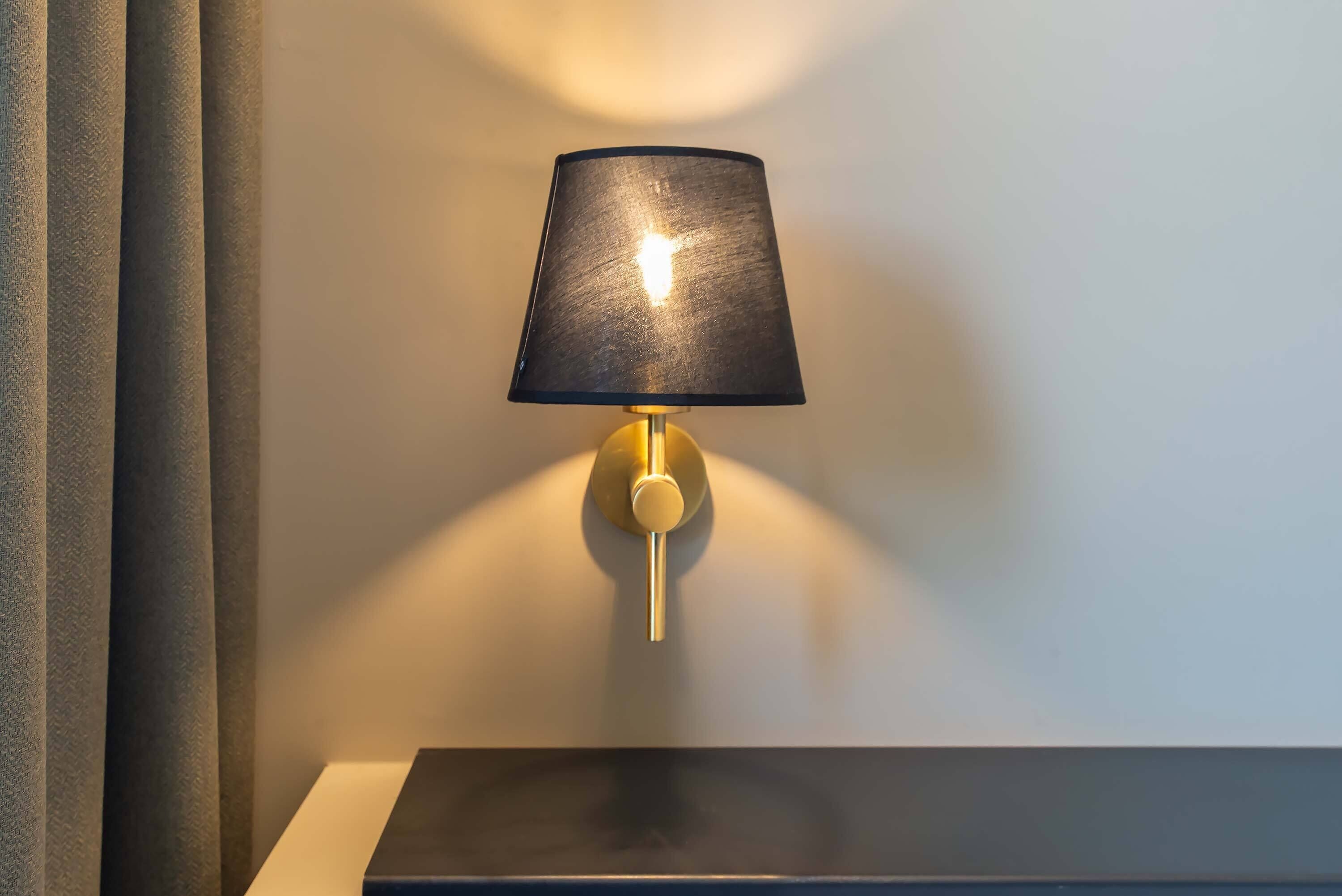 Eine Wandleuchte mit schwarzem Lampenschirm und goldfarbenem Fuß.
