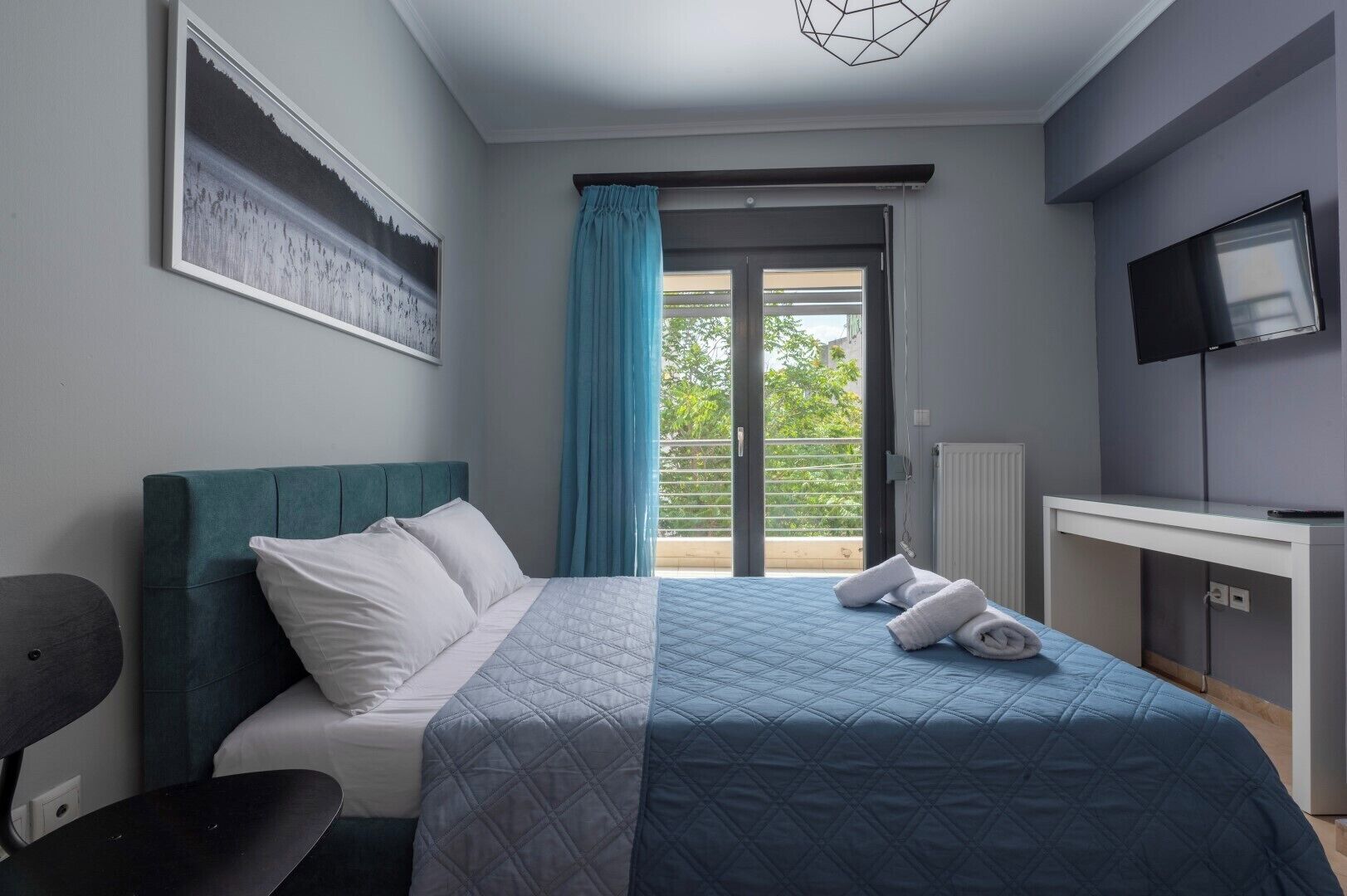 A bedroom with a bed, a desk, a TV, and a window with curtains.