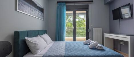 A bedroom with a bed, a desk, a TV, and a window with curtains.