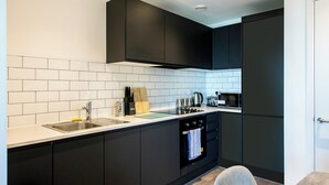 A modern kitchen with black cabinets, white tiles, a stainless steel sink, and a built-in oven. - Insignia Aparment  (Manchester)