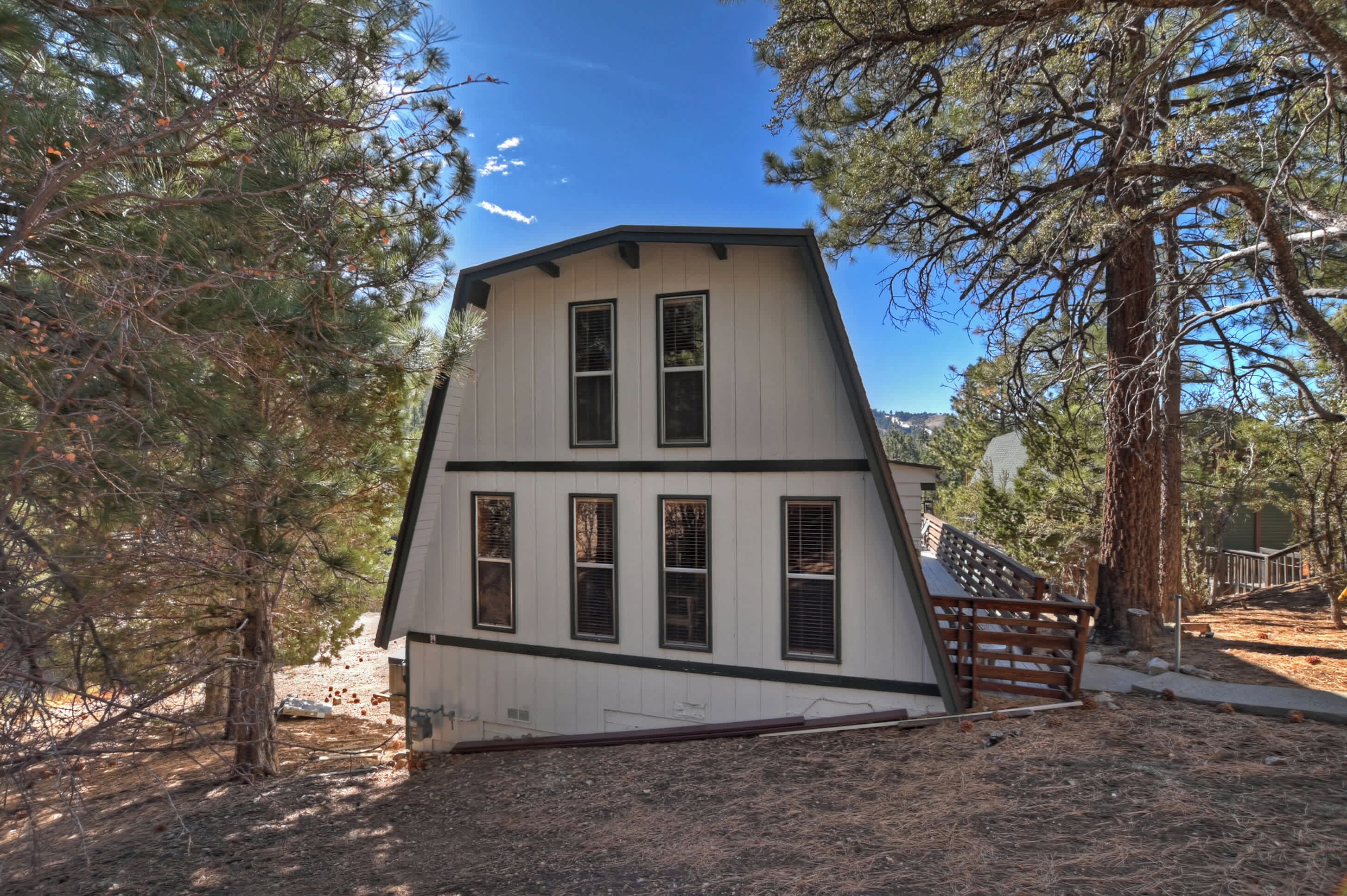 A two-story house with a sloped roof, surrounded by trees and a wooden deck.