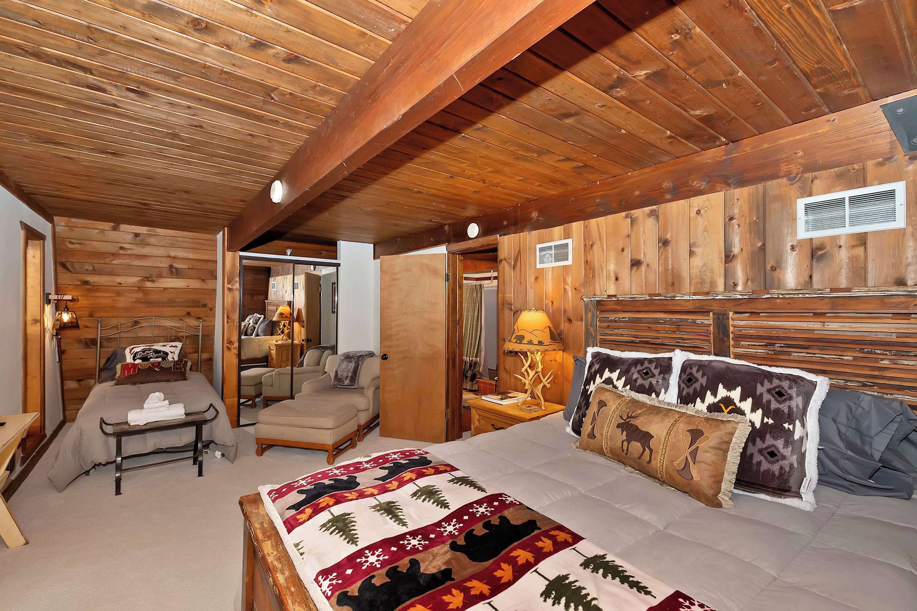 A cozy bedroom with a wooden ceiling, a bed with a quilt, a bedside table with a lamp, and a chair.