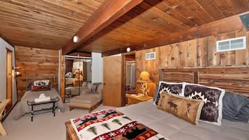 A cozy bedroom with a wooden ceiling, a bed with a quilt, a bedside table with a lamp, and a chair.