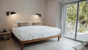 Slaapkamer met een groot bed, twee wandlampen, een klein rond tafeltje en uitzicht op groen buiten.