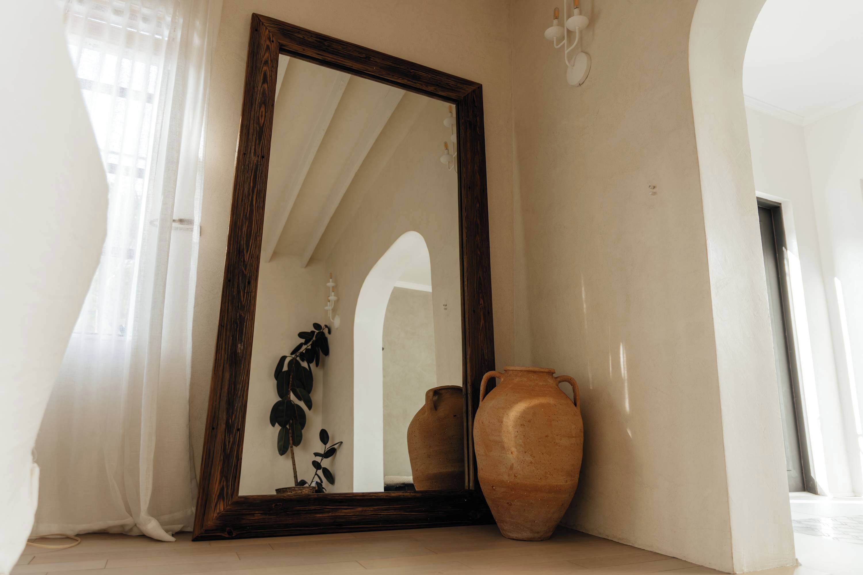 A room with a large mirror, two ceramic vases, and a plant.