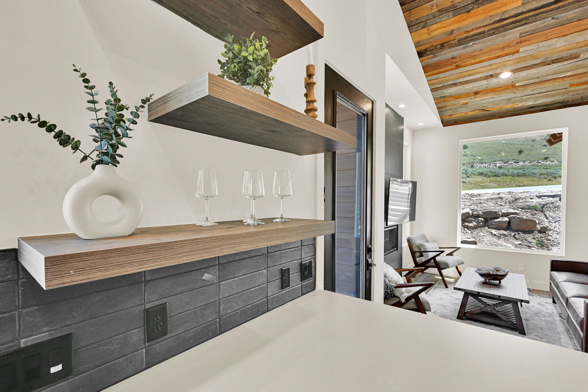 Una cocina moderna con estante de madera, planta en maceta y copas de vino.
