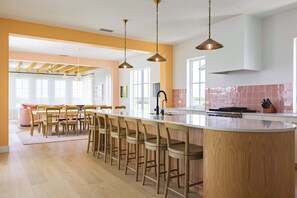 A modern kitchen with a central island, bar stools, pendant lighting, and a large window providing natural light.