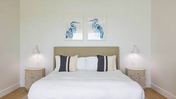 Een keurig opgemaakt bed met een houten hoofdbord, twee nachtkastjes met lampen en twee wanddecoraties van vogels.