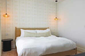 A neatly made bed with a wooden headboard, two bedside lamps, and a small round table beside it. - The Dreamside House at Lunara Bay (Key West)