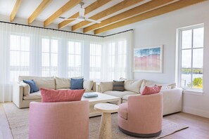 Ein modernes Wohnzimmer mit einem beigen Sofa, zwei rosafarbenen Sesseln, einem kleinen weißen Couchtisch und einem großen Fenster mit transparenten Vorhängen.