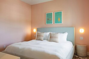 Una cama bien hecha con ropa blanca y almohadillas estampadas, un cabecero azul claro y dos lámparas fijadas a la pared.