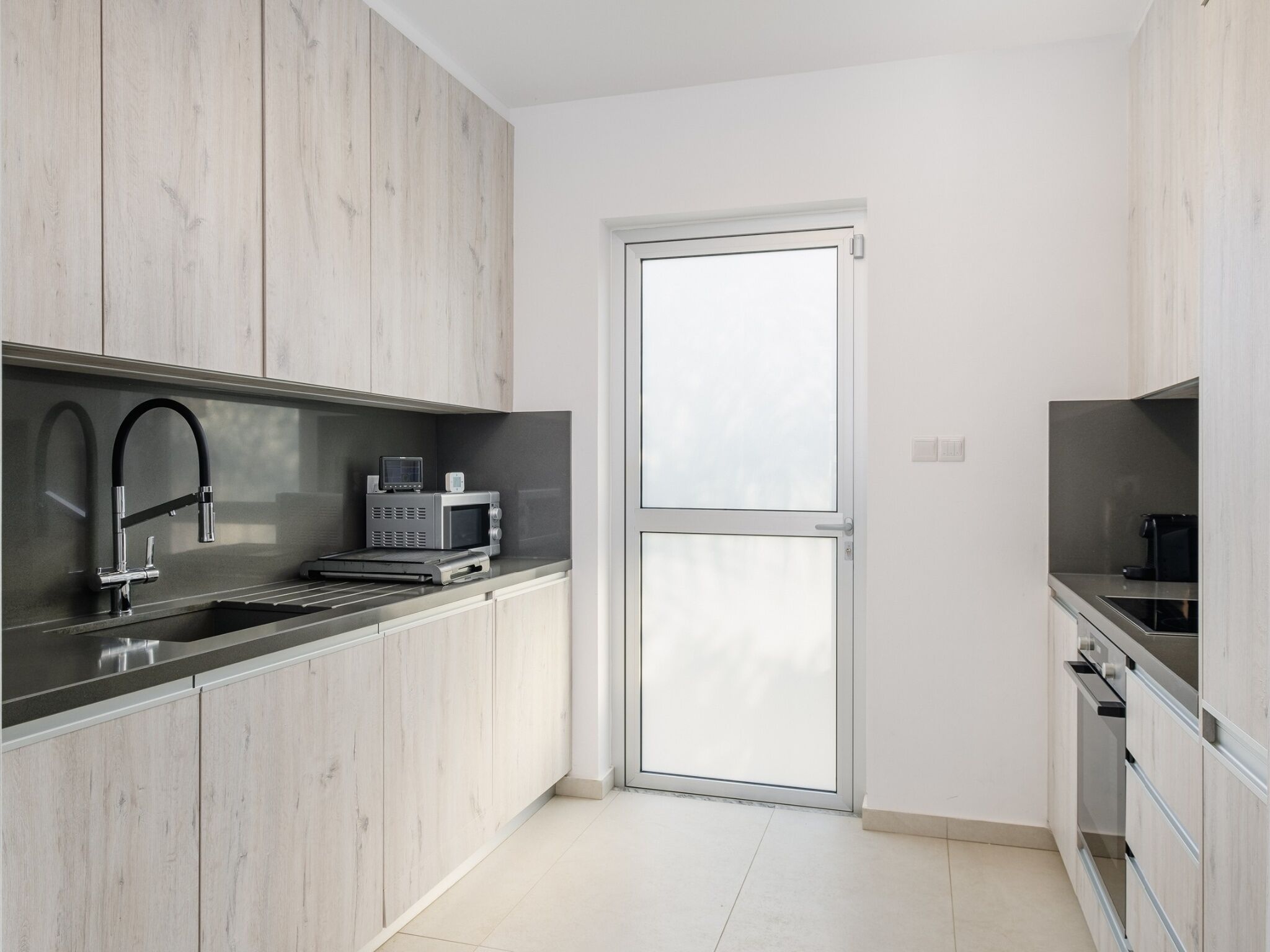 A modern kitchen with a black sink, stainless steel appliances, and light wood cabinetry.