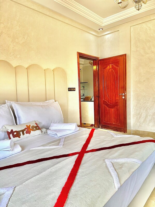A neatly made bed with white linens and a red accent, a wooden door with a mirror, and a chandelier. - Royal home Marrakech (Marrakech)