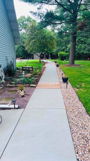 A residential driveway leading to a house with a garden, a wooden deck, and a lawn.