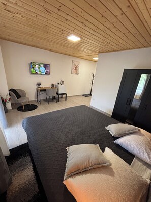 A bedroom with a large bed, a desk, a chair, a TV, and a wardrobe. - Estate Pavlić (Rakovica)
