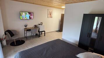 Un dormitorio con una cama grande, un escritorio, una silla, un televisor y un armario.