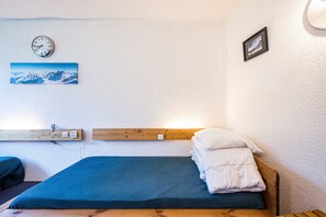 Un lit simple avec une tête de lit en bois, une horloge murale, un tableau encadré et une prise de courant.