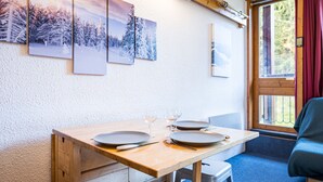 A dining table with plates, cutlery, and glasses, a wooden bench, a window with curtains, and a wall with framed pictures. - Apartment 'Au Coeur De La Station' with Balcony and Wi-Fi (Arc 1800)