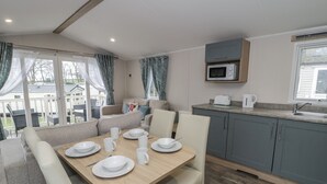 A cozy room with a dining table set for four, a kitchen with a microwave and toaster, and a seating area with a sofa and chairs. - Woodlands Platinum (Ruthin)