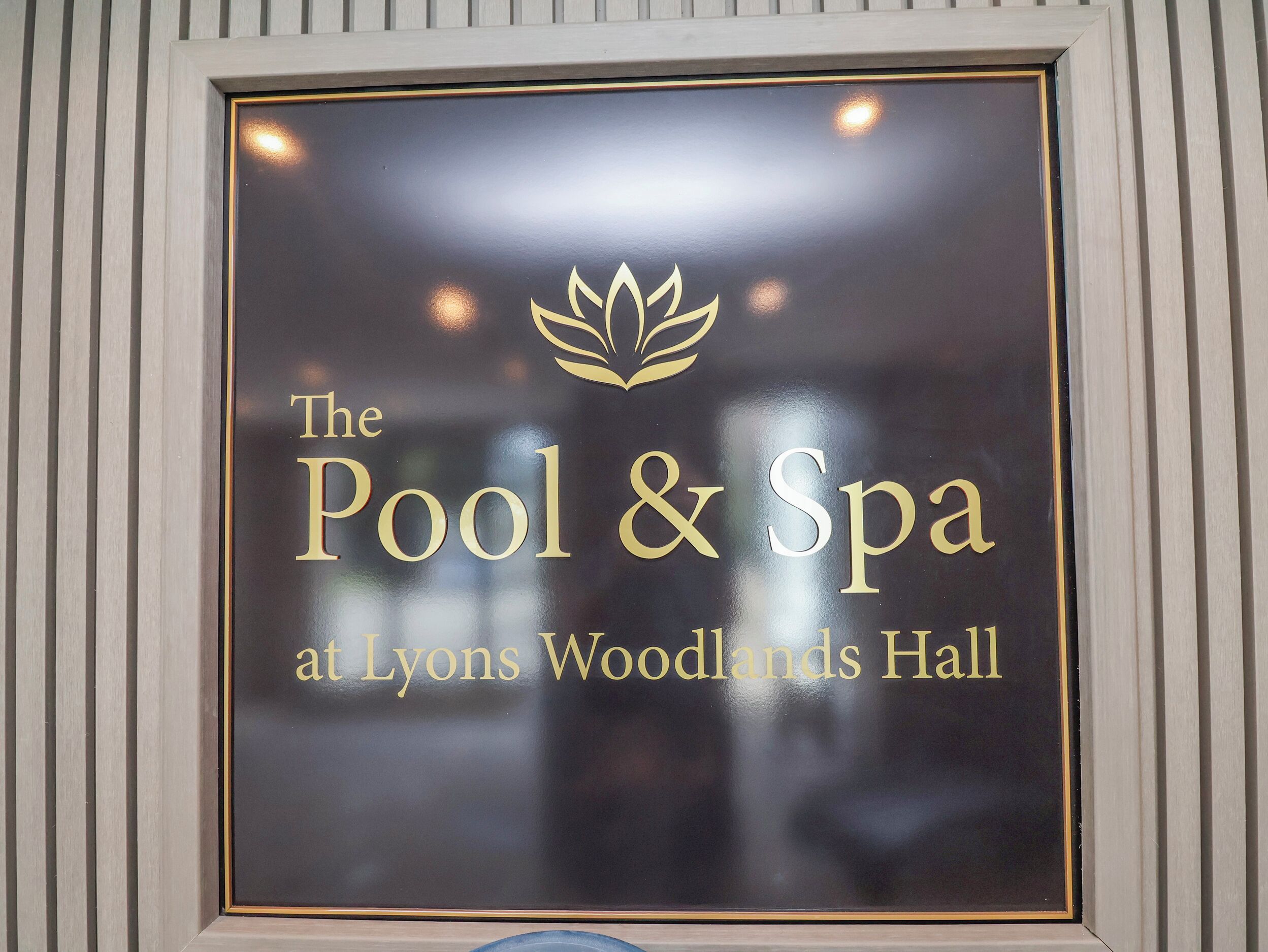 Señal que indica 'La Piscina y el Spa en Lyons Woodlands Hall' con un logo de hoja.