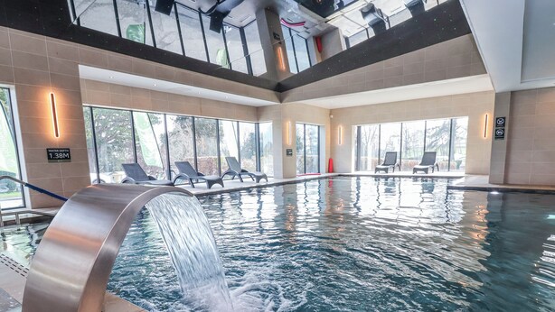 Une piscine intérieure agrémentée d’une cascade, de chaises longues et de grandes fenêtres.