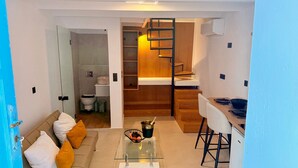Um espaço compacto com cozinha compacta, mesa de centro de vidro, sofá com almofadas e escada de madeira.