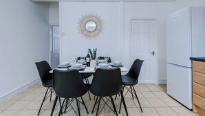 A dining area with a white table set for four, black chairs, a gold mirror on the wall, and a white refrigerator to the right.