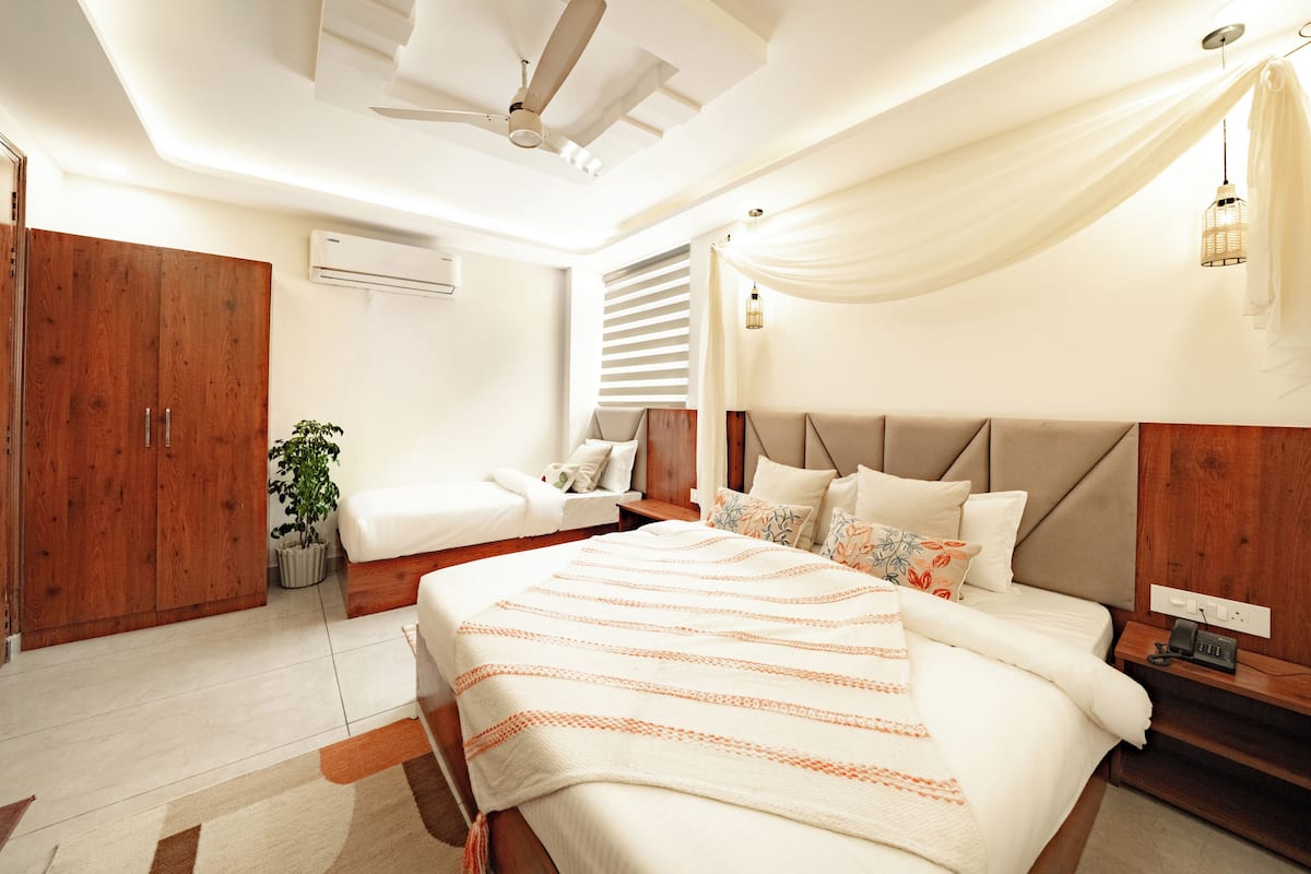 A modern bedroom with a large bed, a smaller sofa, wooden wardrobe, and a ceiling fan.