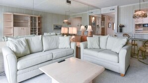 A modern living room with two light-colored sofas, a coffee table, and a dining area with a table and chairs.