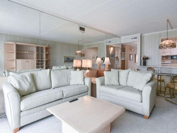 A modern living room with two light-colored sofas, a coffee table, and a dining area with a table and chairs.