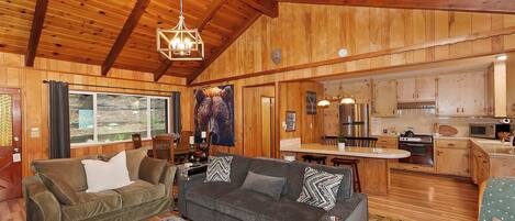 A cozy cabin interior with a wooden ceiling, a dining area, and a kitchen.