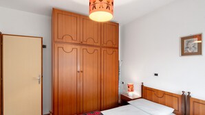 Quarto com cama, guarda-roupa, mesa de cabeceira e luminária suspensa.