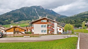 Uma aldeia de montanha com casas de madeira tradicionais, uma estrada pavimentada e uma montanha ao fundo.