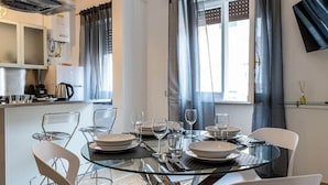 Un espace repas moderne avec une table en verre, des chaises blanches et une cuisine en arrière-plan.