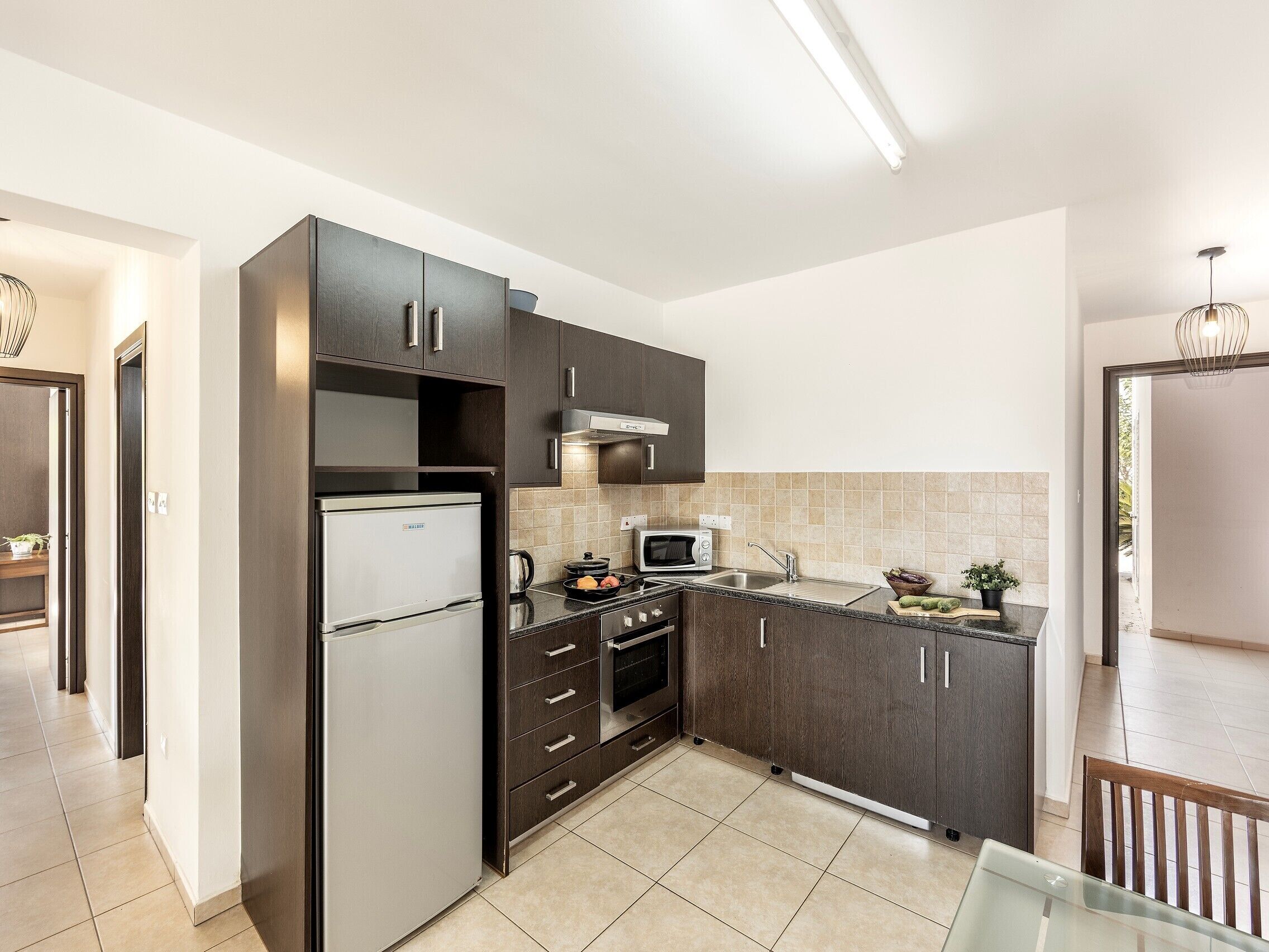 A modern kitchen with dark cabinetry, a stainless steel refrigerator, a microwave, and a sink.