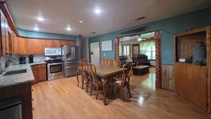 A spacious kitchen with wooden cabinets, a dining table with chairs, and a living area with a couch and a fireplace. - Charming 4-bedroom Country Home near Canton, TX (Edgewood)