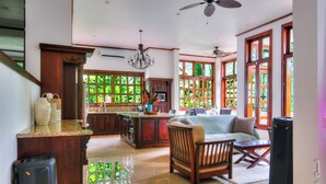 A spacious living area with a kitchen, a dining area, and a seating area with a sofa and chairs. There is a large window with a view of greenery outside. - Beautiful & Exclusive Garden Villa - Privacy, Security, Pool, Jacuzzi (Quebrada Ganado)