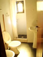 Un baño pequeño con dos inodoros, un lavabo y zona de ducha.