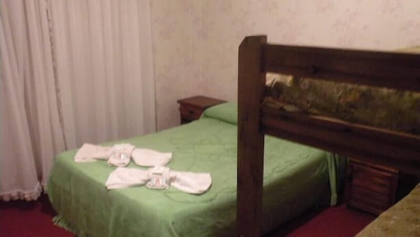 Una cama individual con una colcha verde y un cabecero de madera. Hay toallas sobre la cama.